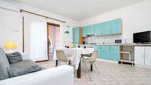 Eine moderne Küche mit türkis-blauen Schränken, einem Esstisch und einem Fernseher.