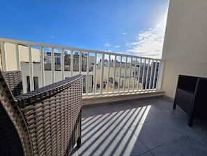 A balcony with a white railing, wicker furniture, and a view of buildings in the background. - Msida 2 Terraces 2 Bedrooms, 2 Bathrooms Family Friendly (L-Imsida)