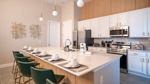 A modern kitchen with white cabinets, stainless steel appliances, and a central island with bar stools. - 11BR Luxury Villa w/ Pool Near Disney (Orlando)