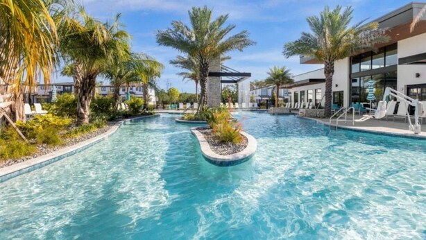 A swimming pool with palm trees and lounge chairs, surrounded by buildings. - 11BR Luxury Villa w/ Pool Near Disney (Orlando)