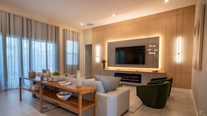 A modern living room with a sofa, a coffee table, a TV, and a fireplace. - 11BR Luxury Villa w/ Pool Near Disney (Orlando)