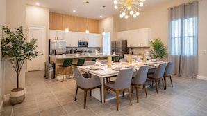 A modern kitchen with white cabinets, stainless steel appliances, and a dining area with a table set for six. - 11BR Luxury Villa w/ Pool Near Disney (Orlando)