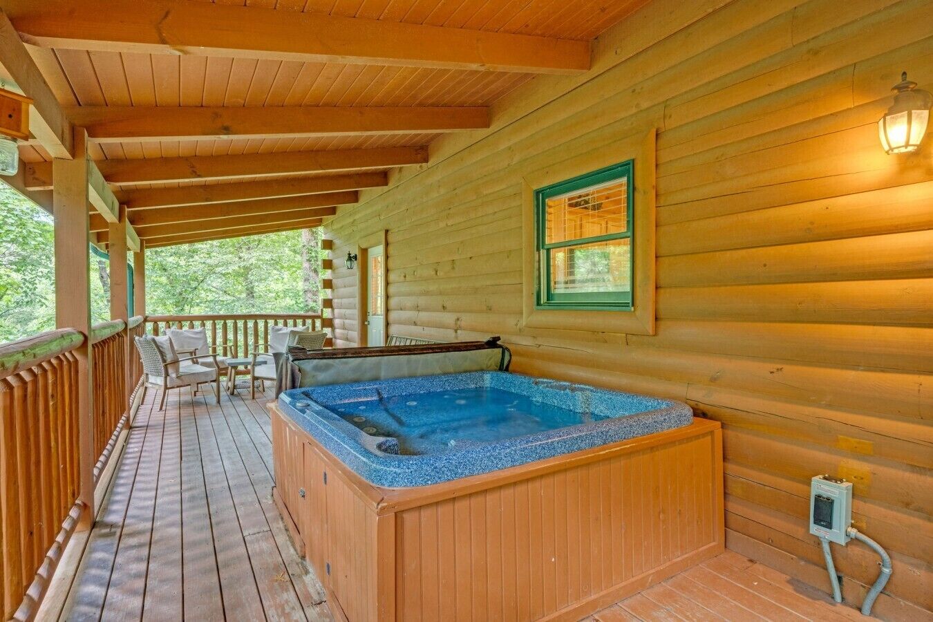Eine Holzhütte mit einem Whirlpool auf einer Terrasse, einem Fenster mit Rollläden und einem Holzgeländer.