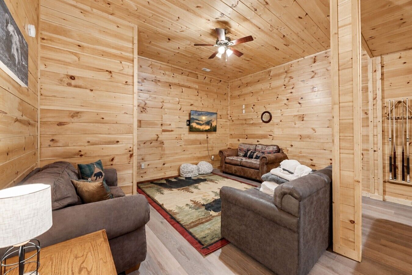 Interno di una baita in legno con un divano, un divanetto, un tappeto e una ventola a soffitto.