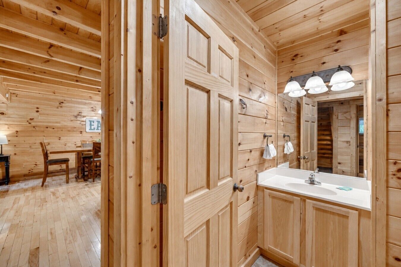 Interno di una baita in legno con una porta di legno, un lavandino e uno specchio.
