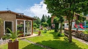 Un jardin avec une piscine, une terrasse en bois et une maison en briques.