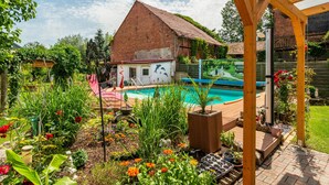 Un jardin avec une piscine, une pergola en bois et diverses plantes.