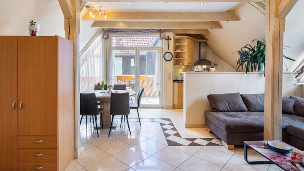 Une cuisine moderne avec des poutres en bois, un coin repas avec des chaises, un canapé et une vue à travers une porte vitrée.