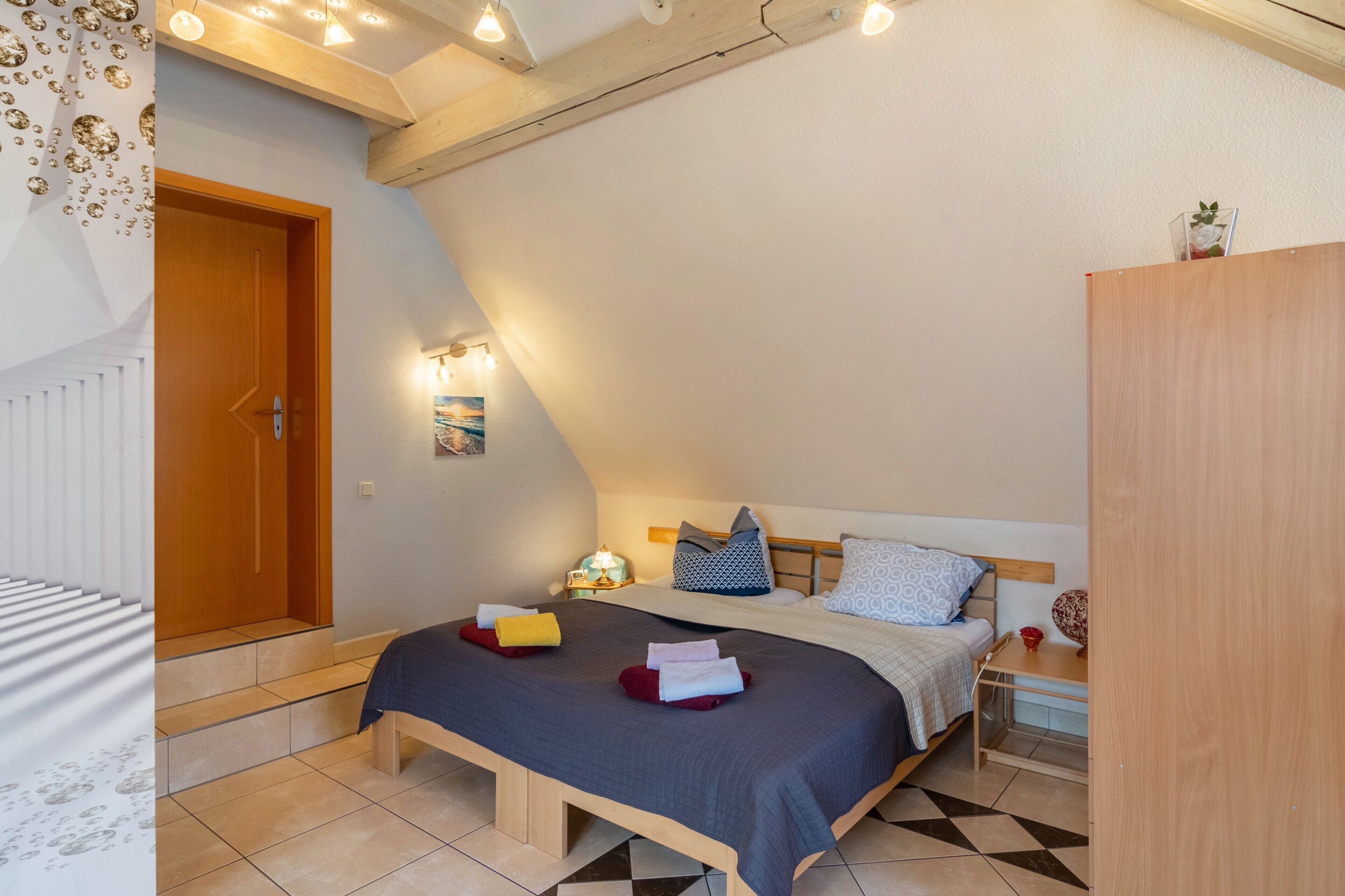 A bedroom with a bed, bedside table, lamp, and a view of the outside.