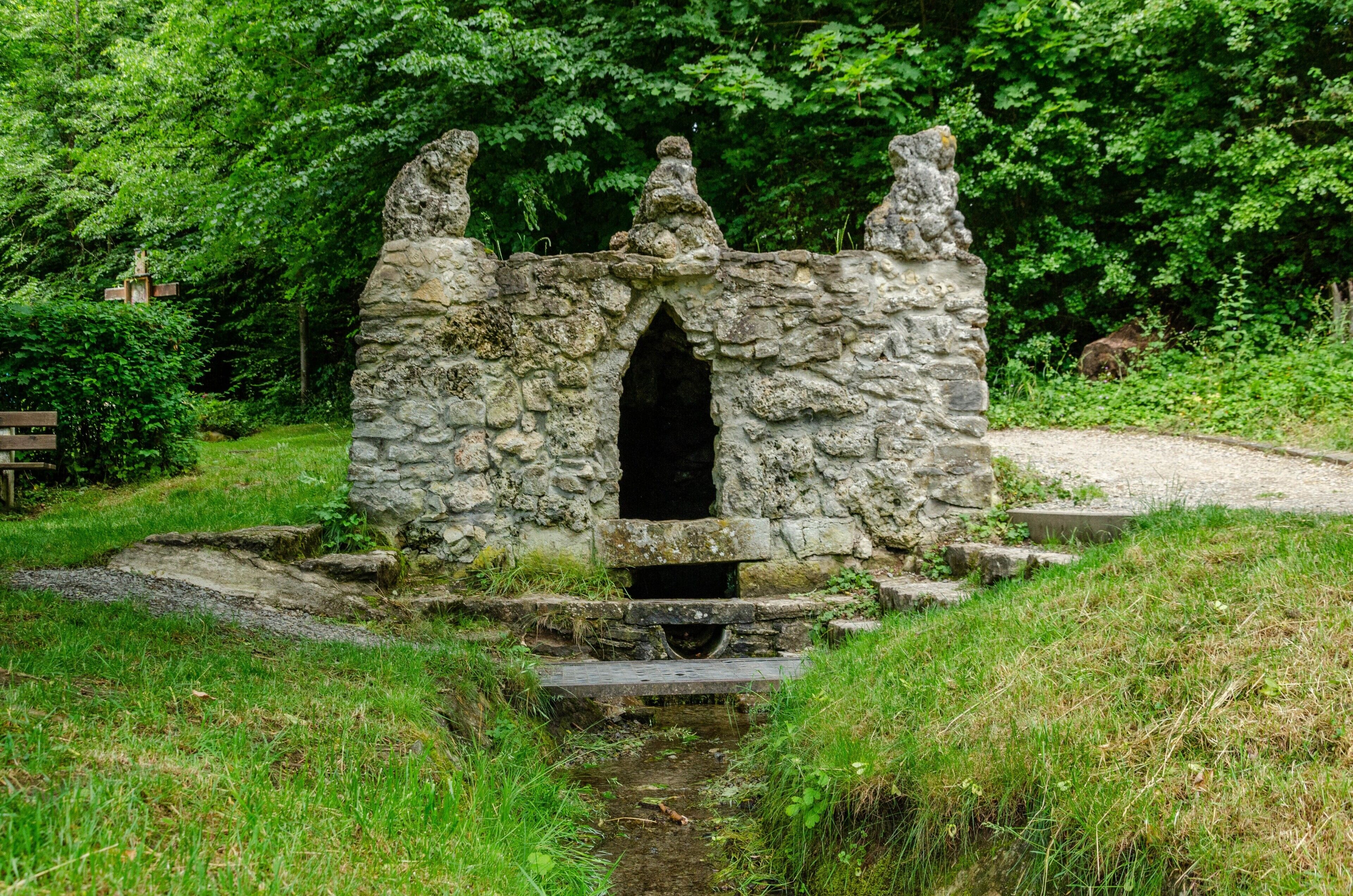 Estrutura de pedra com um arco central, rodeada por vegetação.