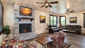 A cozy living room with a fireplace, leather sofas, a patterned armchair, and a ceiling fan. - Creekside Paradise: Hot Tub,Arcade Games,NEAR PF! (Pigeon Forge)