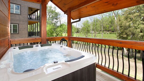 A hot tub on a wooden deck with a view of a house and trees. - Creekside Paradise: Hot Tub,Arcade Games,NEAR PF! (Pigeon Forge)