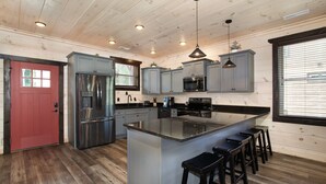 A kitchen with wooden walls, a red door, stainless steel appliances, and bar stools. - Creekside Paradise: Hot Tub,Arcade Games,NEAR PF! (Pigeon Forge)