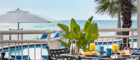 A balcony with a table set for breakfast, overlooking a pool and the ocean.