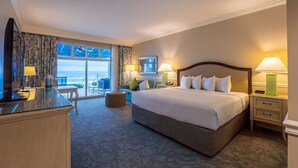 Een hotelkamer met een groot bed, een bureau, een stoel, een kleine tafel en uitzicht op de oceaan.