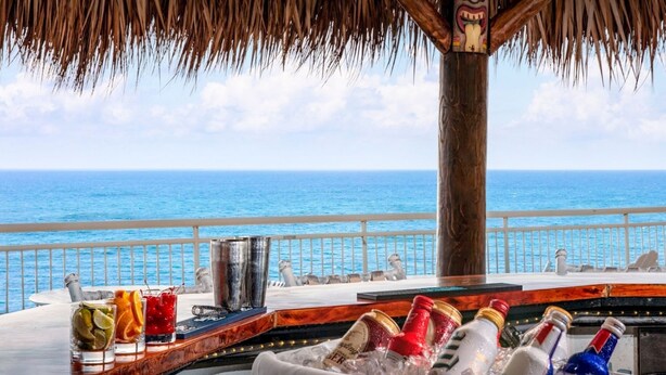 Een bar met uitzicht op de oceaan, een rieten dak en een tiki-beeldje.
