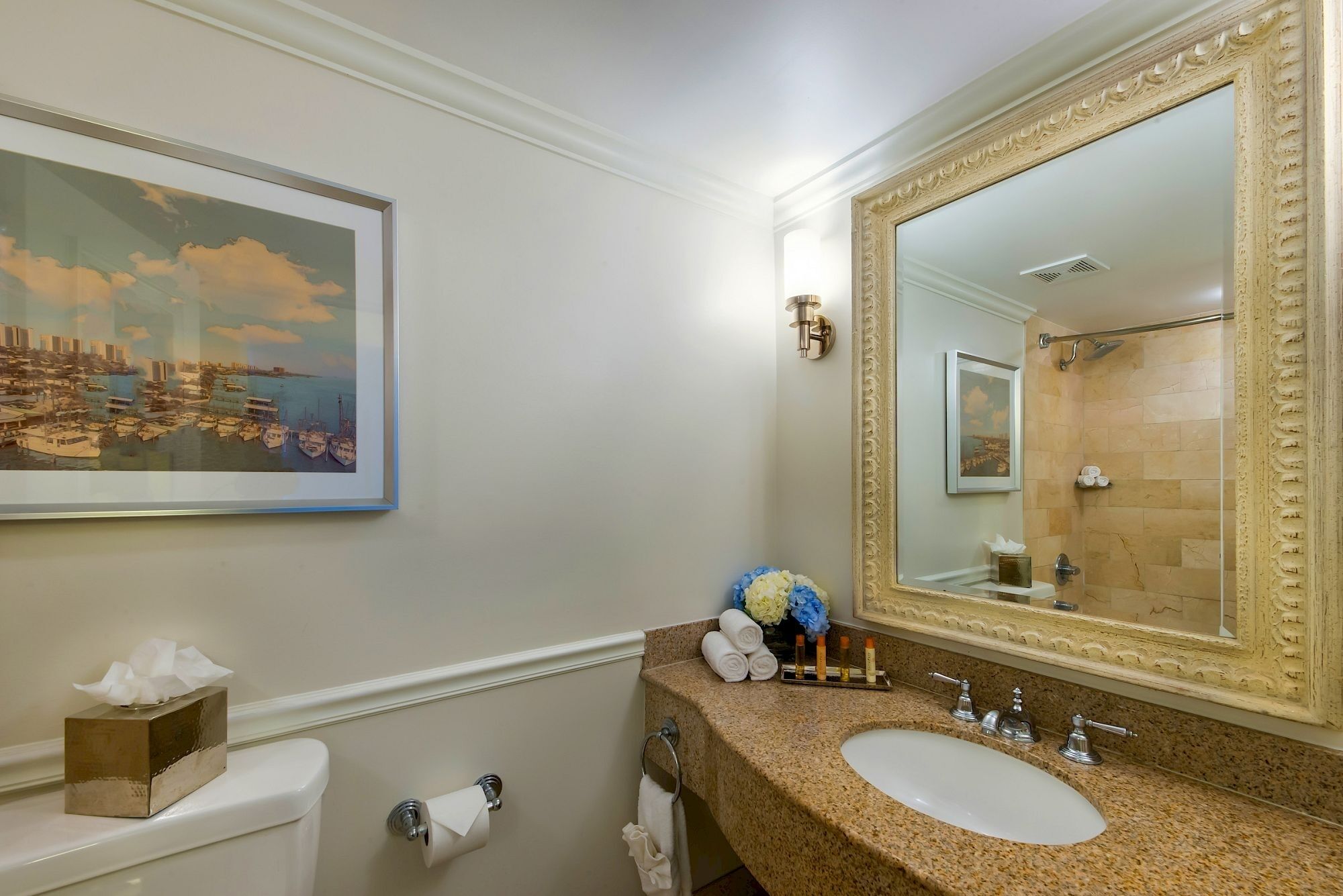 A bathroom with a large mirror, a sink, a toilet, and a framed painting on the wall.