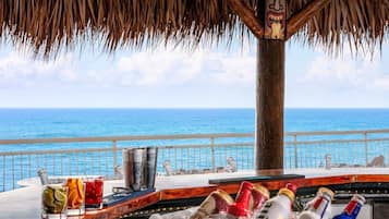 A bar area with a view of the ocean, a thatched roof, and a tiki statue.