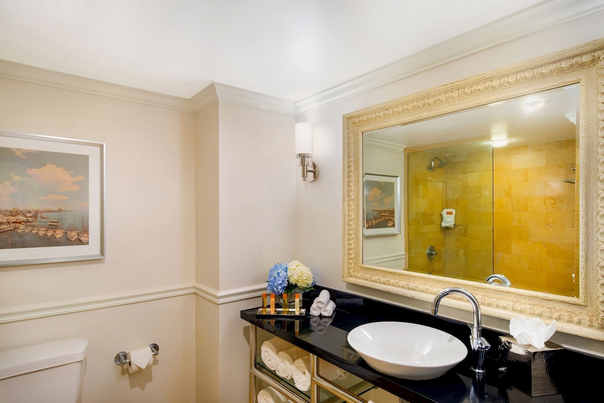 Ein Badezimmer mit einem großen Spiegel, einem Waschbecken, einer Toilette und einem gerahmten Bild an der Wand.