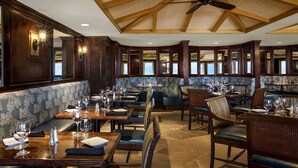 Un restaurante con techos de madera altos, un ventilador de techo y una combinación de cabinas y mesas dispuestas con copas de vino.