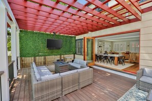 Une terrasse extĂ©rieure dotĂ©e dâune pergola rouge, dâun tĂ©lĂ©viseur Ă Ă©cran plat, dâun foyer et dâun espace repas avec une table et des chaises.