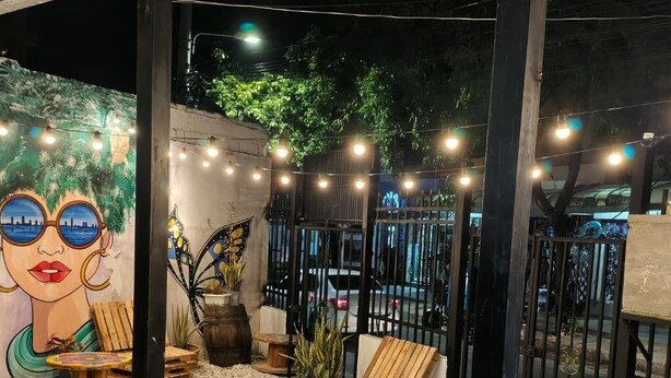 An outdoor seating area with wooden furniture, string lights, and a mural. - Nomadas hostels (Santa Marta)