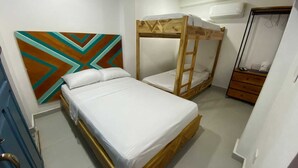 A bedroom with a bunk bed, a single bed, a dresser, and a wall with a geometric pattern. - Nomadas hostels (Santa Marta)