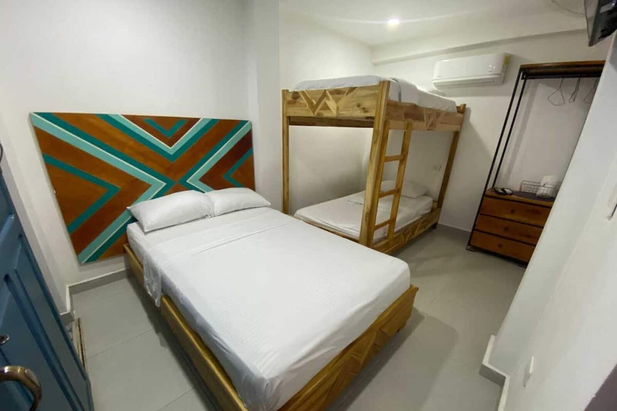 Une chambre avec un lit superposé, un lit simple, une commode et un mur orné d’un motif géométrique.