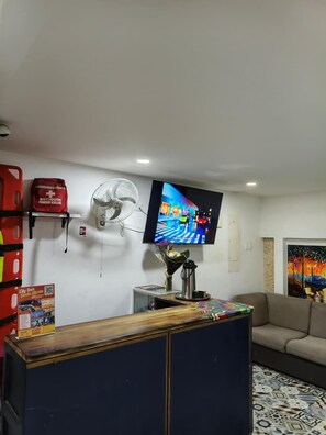 Een kamer met een televisie, een ventilator, een bank, een salontafel en een schilderij aan de muur.