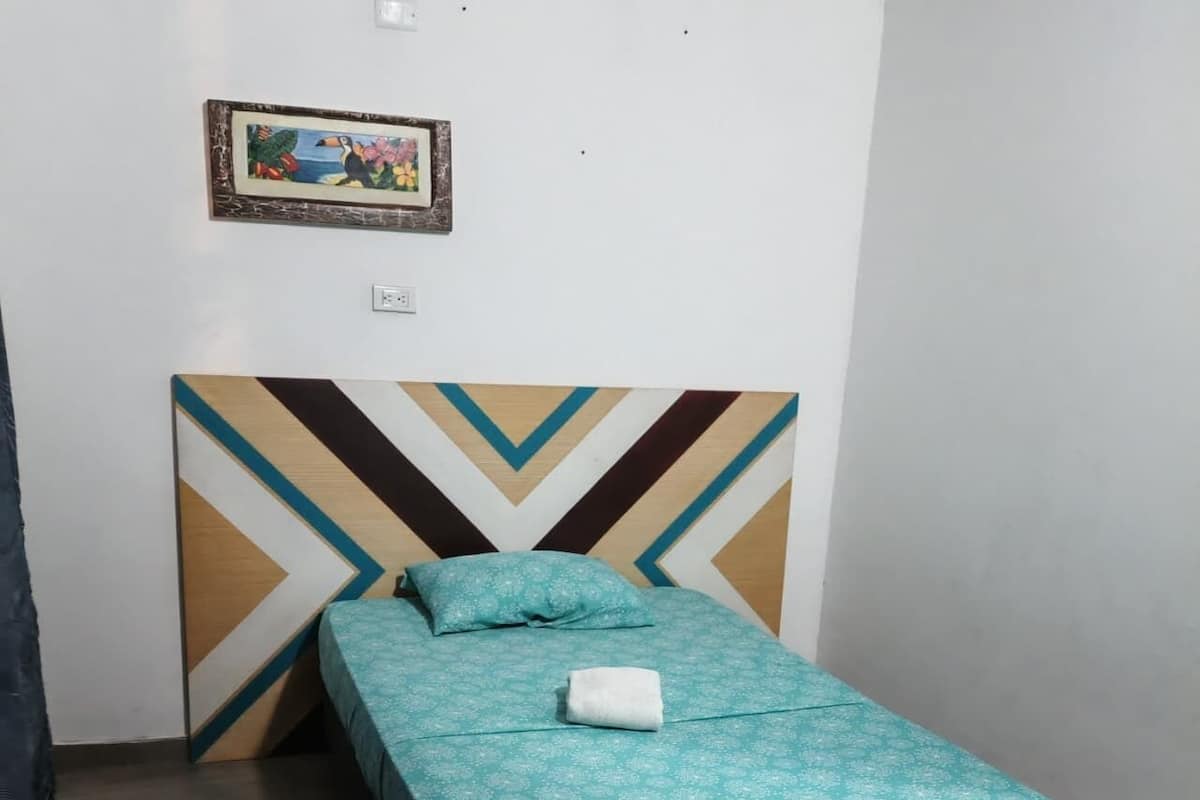 Un lit simple avec une couvre-lit à motifs, un oreiller et une serviette pliée, le tout posé sur un cadre noir.
