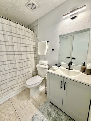 A bathroom with a toilet, a sink, a mirror, and a shower curtain. - King Suite Full Kitchen Near Airport & Downtown (Tampa)