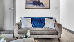 Un salon moderne avec un canapé gris, un plaid bleu et un tableau accroché au mur.