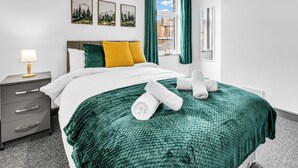 En pænt redt seng med et grønt tæppe, en sengetavlelampe og et natbord med skuffer.