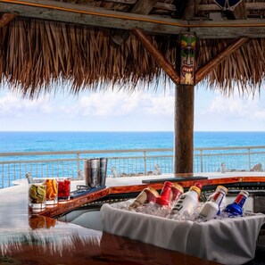 Eine Bar mit Meerblick, einem Reetdach und einer Tiki-Statue.