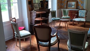 Una habitación con suelo de madera, varias sillas, una mesa, un espejo y papel tapiz con motivos florales.