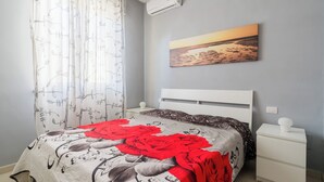 A bedroom with a bed, a nightstand, a wall-mounted air conditioner, and a painting of a sunset. - Villa Miglietta by BarbaHouse (Torre Lapillo)
