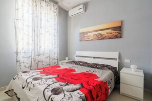 Ein Schlafzimmer mit einem Bett, einem Nachttisch, einer Wand-Klimaanlage und einem Sonnenuntergangsbild.