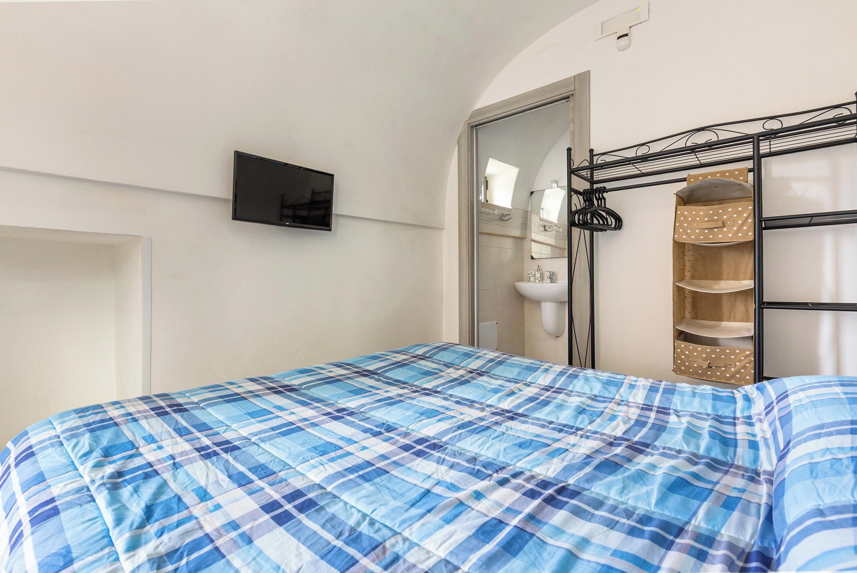 Ein Schlafzimmer mit einem Bett, einem an der Wand montierten Fernseher, einem Spiegel und einem Regal mit Aufbewahrungsboxen.