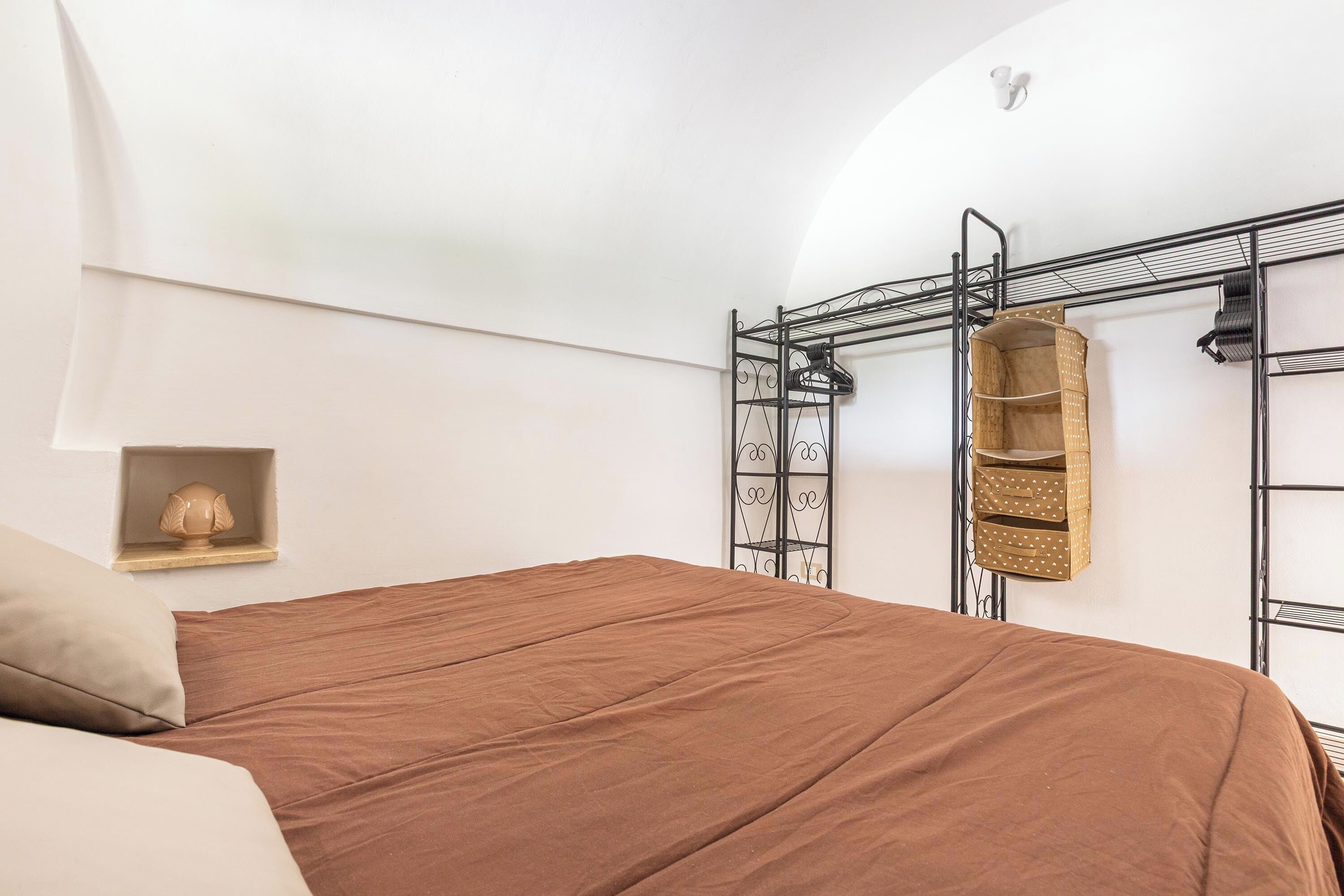 Une chambre à coucher avec un lit, une étagère ornée d’un objet décoratif et un présentoir en métal avec des paniers.