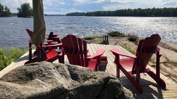 Une terrasse en bois avec des fauteuils Adirondack rouges donnant sur un lac.