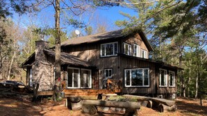 Un chalet rustique avec une cheminée en pierre, de grandes fenêtres et une terrasse en bois.