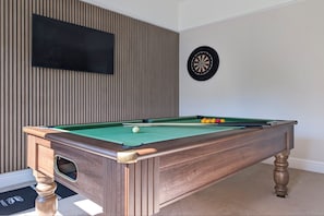 A pool table with a dartboard and a TV mounted on a wooden wall. - Rosemount Boutique (Windermere)