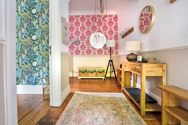 A room with a wooden floor, a bench, a desk with a lamp, and a wall with floral wallpaper. - Rosemount Boutique (Windermere)