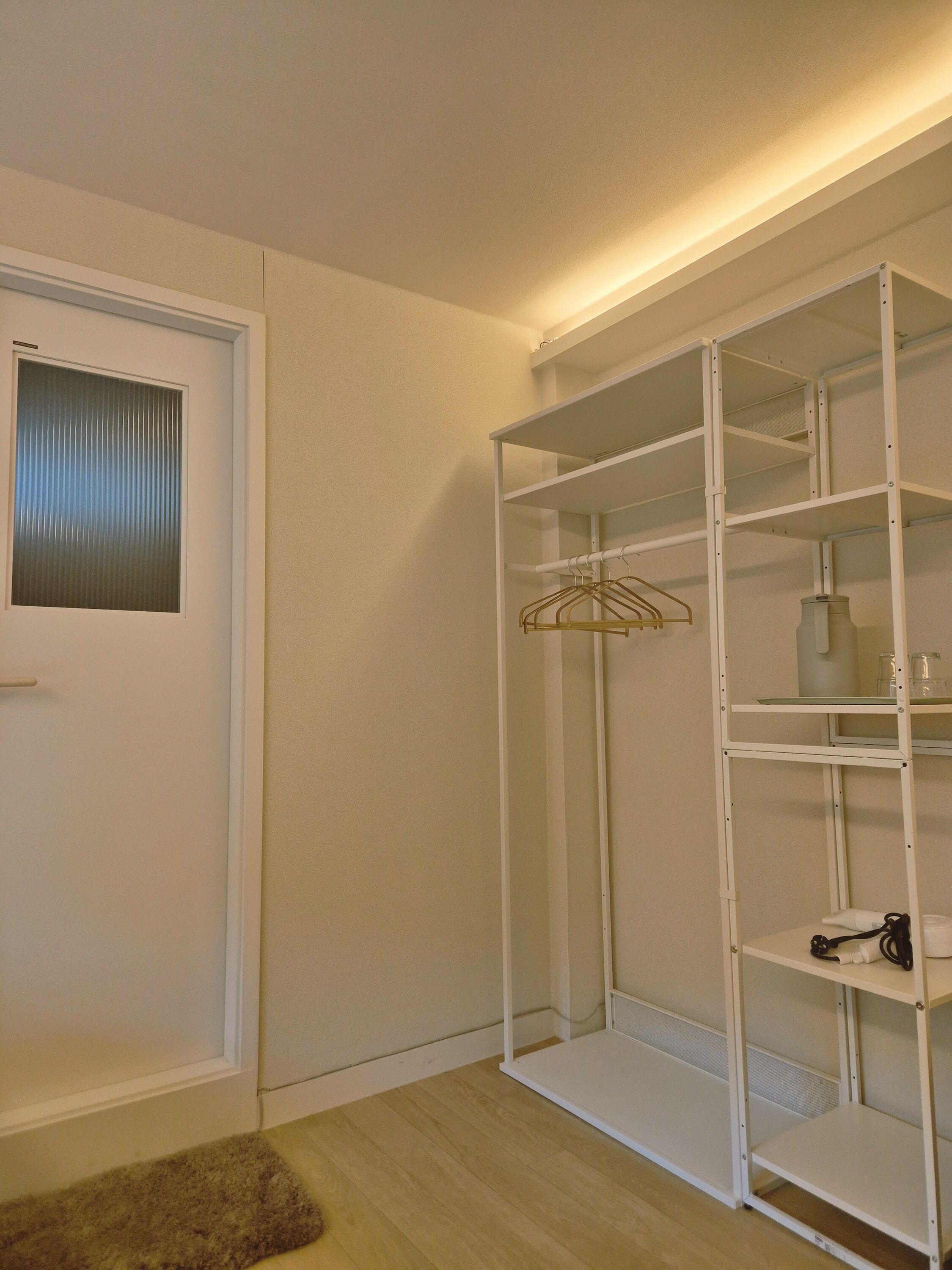 A white closet with shelves and a hanging rod, a door with a window, and a wooden floor.