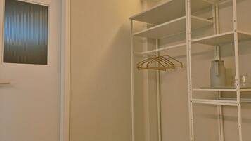 A white closet with shelves and a hanging rod, a door with a window, and a wooden floor.