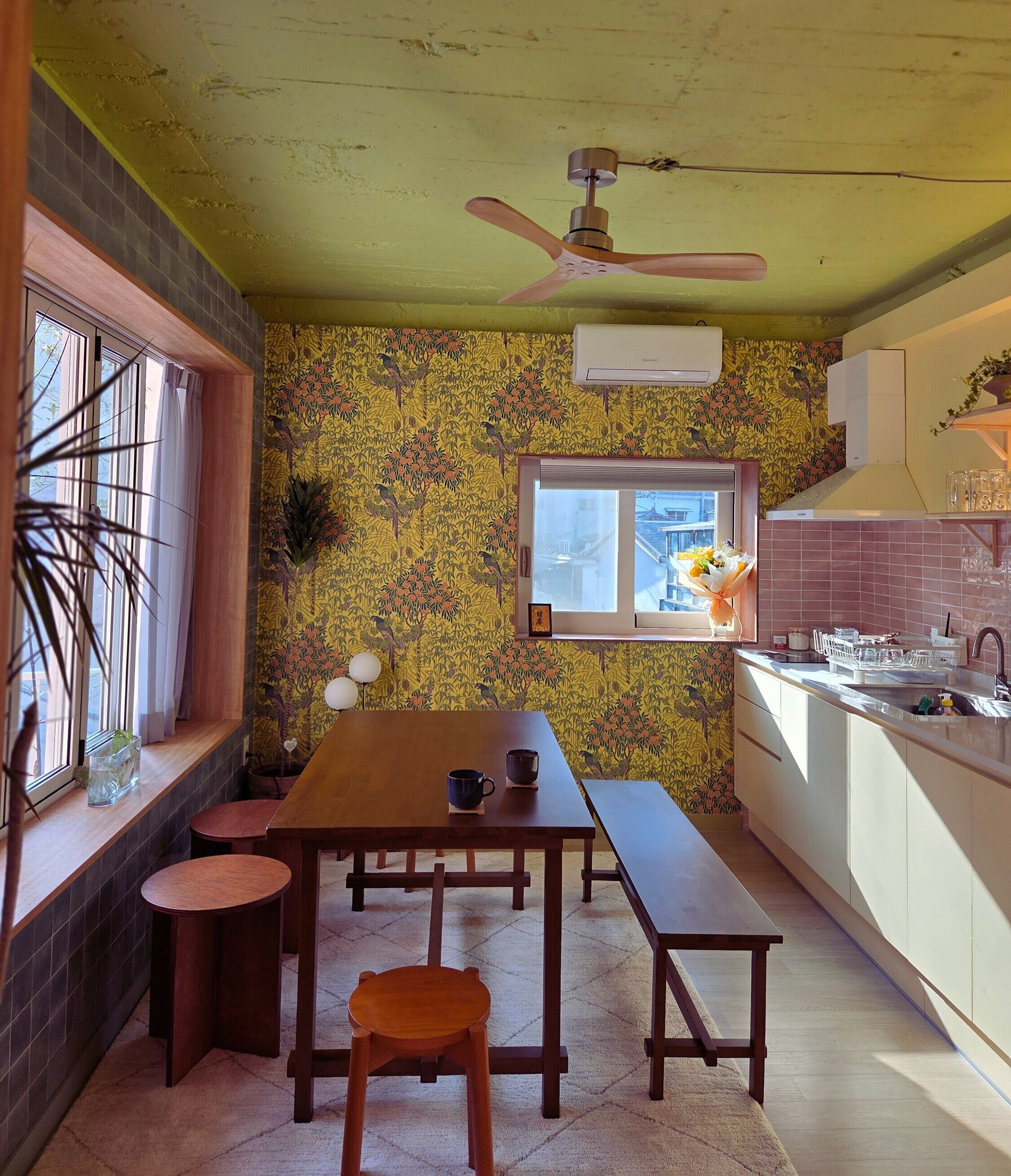 A compact kitchen with a dining area, a ceiling fan, a window with a view, and a tiled backsplash.