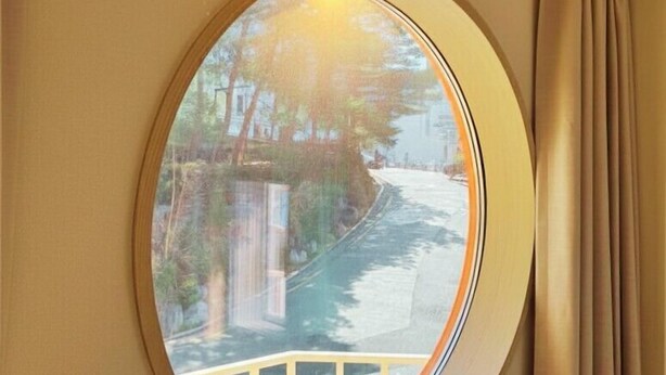 A round window with a view of a tree-lined street. - SoSi Stay (Seoul)