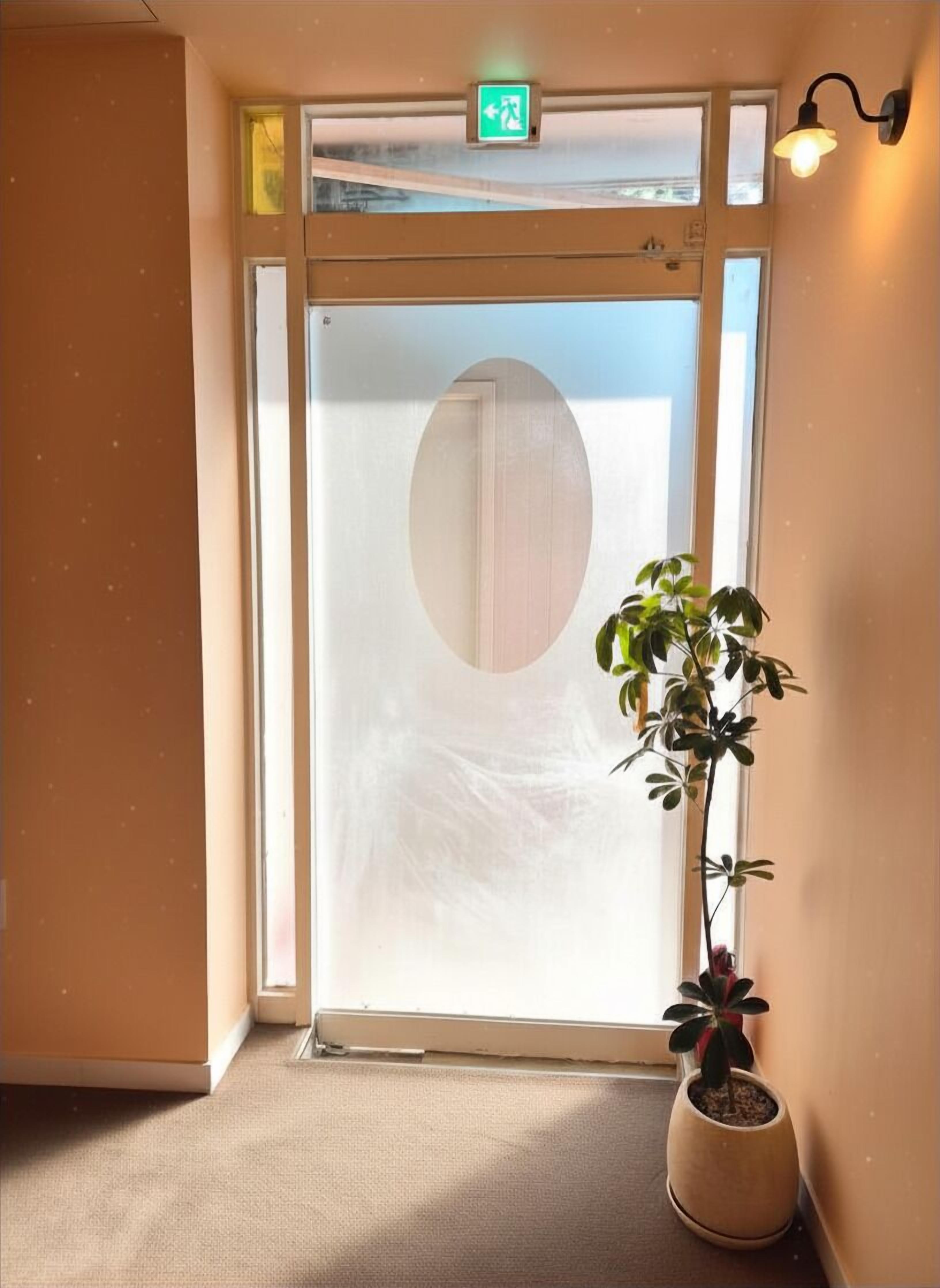 A hotel entrance with a frosted glass door, a potted plant, and a wall-mounted light fixture.