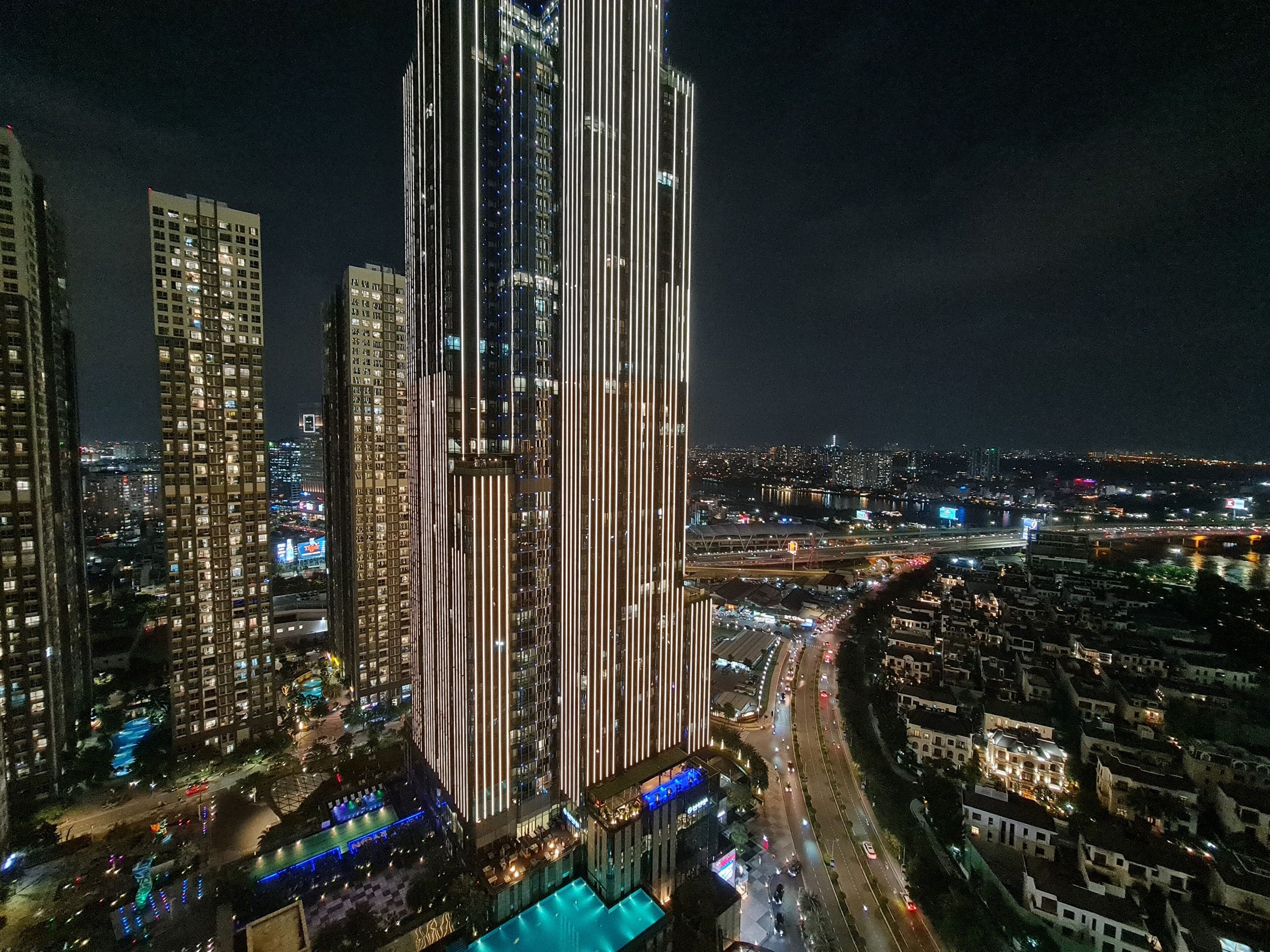 Ein Wolkenkratzer mit vertikalen Lichtleisten, einem Schwimmbad und einer belebten Straße.