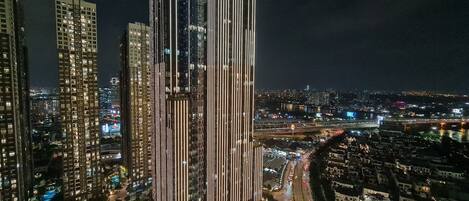 Un edificio de gran altura con líneas verticales de luces, una piscina y una calle concurrida.